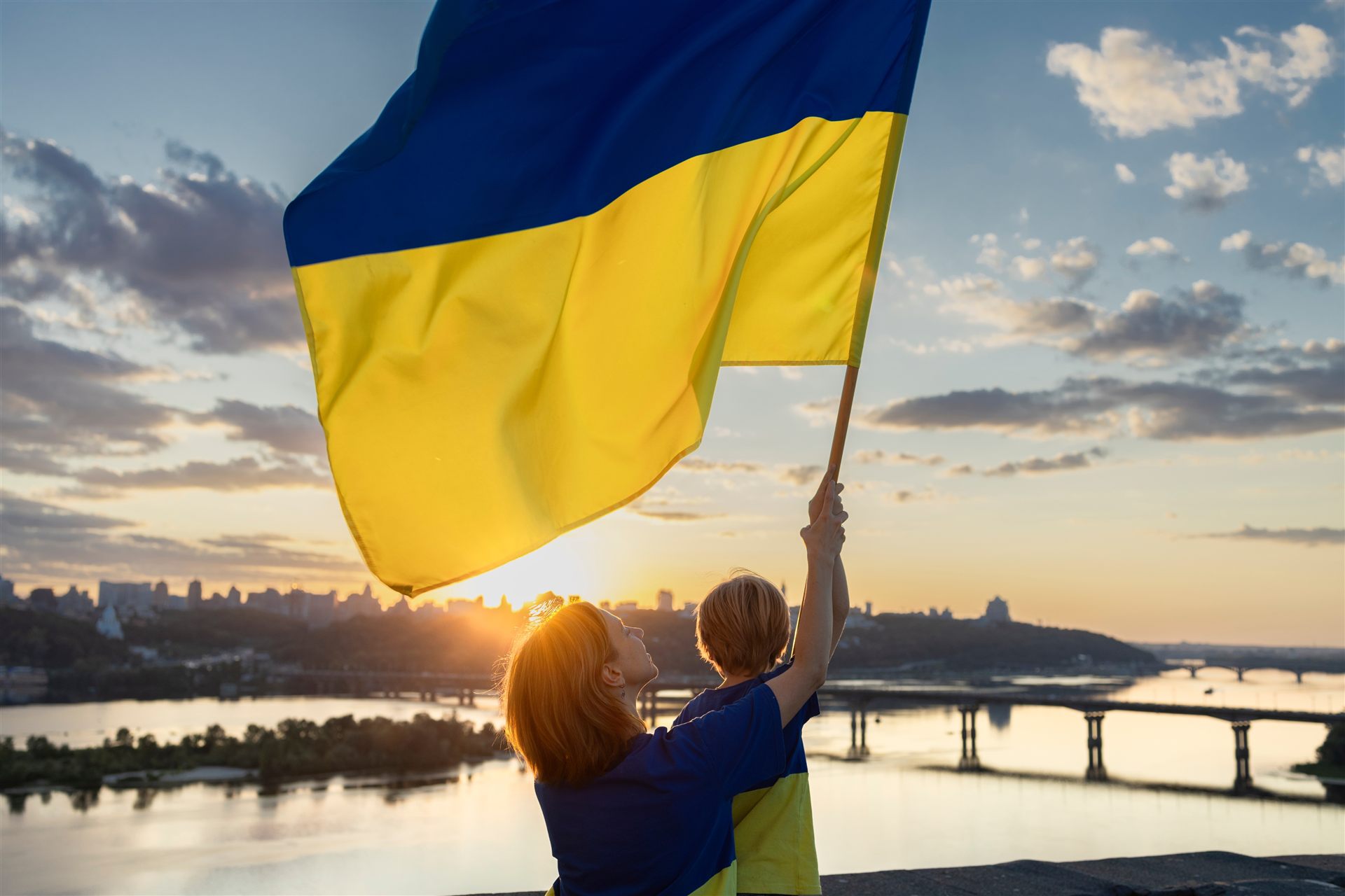 Mutter und Kind mit ukrainischer Flagge bei Sonnenuntergang über Kyjiw